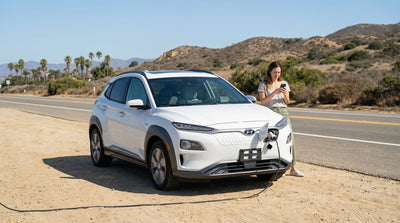 A modern electric car hire pulled over on a scenic, winding California highway with mountains in the background