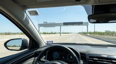 A car rental drives under a highway toll gantry on a sunny day in Austin, Texas