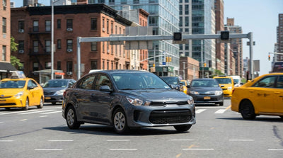 A car rental sits in heavy traffic on a busy New York City street among yellow cabs and tall buildings