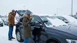 Person using an ice scraper to clear snow from a car rental windshield on a New York street