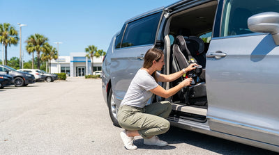 A parent checks a child safety seat in the back of their car rental on a sunny day in Orlando