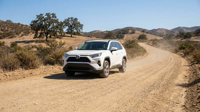 An SUV car hire drives down a dusty dirt road towards scenic mountains in California