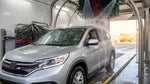 Silver car rental covered in soap and water inside an automatic car wash in Texas