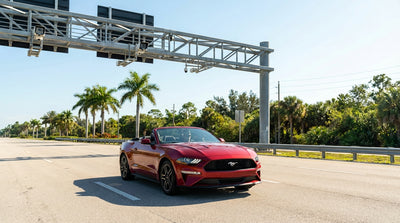 A car rental drives on a sunny Florida highway towards an electronic toll gantry with palm trees