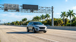 White car rental driving in an express lane on a sunny Florida highway with palm trees