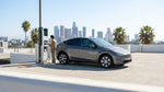 A modern electric car rental plugged into a charging station on a sunny day in Los Angeles