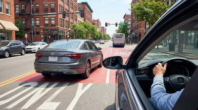 A car hire drives beside a red bus-only lane on a busy city street in Philadelphia, Pennsylvania