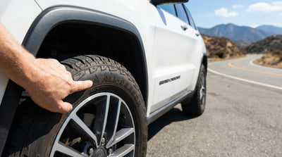 A person checking the tyres of a car rental parked on a scenic mountain road in California
