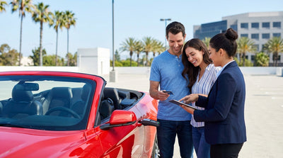 A red convertible car hire driving along a scenic coastal highway in California at sunset