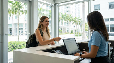 A young driver smiling next to their red convertible car hire on a sunny palm-tree-lined street in Miami
