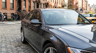A modern car rental drives down a bustling street in New York, with yellow cabs and skyscrapers in the background