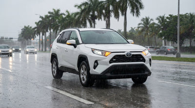 A car rental driving through heavy rain on a freeway in Miami, with streetlights reflecting on the wet road