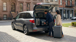 Person loading three large suitcases into the open trunk of a car rental on a New York street