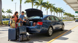 Luggage loaded into the open trunk of a full-size car rental parked near a Florida beach
