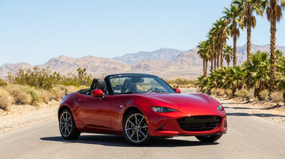 A sports car rental driving down the Las Vegas Strip at dusk with glowing neon casino lights