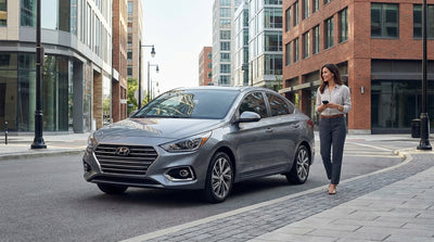 A silver car rental sedan driving on a street in downtown Manhattan, with iconic yellow cabs and tall buildings nearby