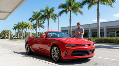 Red convertible car hire driving down a sunny coastal highway lined with palm trees in Florida