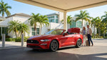 White convertible car rental driving past a sandy beach and palm trees in Miami