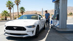Person pumping fuel into a car rental at a sunny California gas station with palm trees