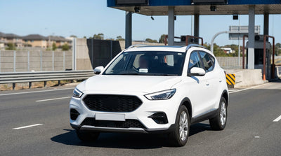 A white car rental driving through an E-ZPass toll gantry on a busy highway in New York