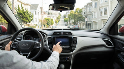 A driver in a car rental taps the infotainment screen with the San Francisco skyline visible through the window
