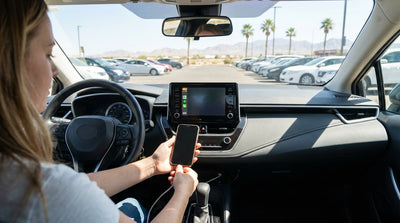 A driver connecting an iPhone to the dashboard screen of a car rental in a sunny Las Vegas parking lot
