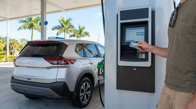A person at a sunny Florida gas station pump holding a credit card to pay for their car rental fuel