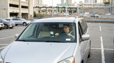A driver holds a smartphone with a map app while in a car rental on a busy street in New York