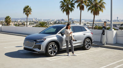 A person plugs in their white electric car rental at a charging station with the Los Angeles Airport in the background