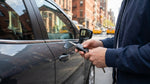 A person's hand holding a car rental key fob with a blurred background of a busy New York City street