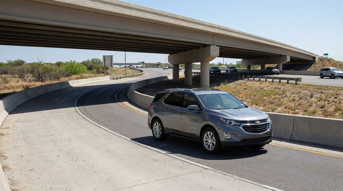 A modern car hire drives on a frontage road in Texas towards a U-turn turnaround lane under an overpass