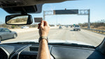 Dashboard view from a car rental approaching an overhead toll gantry on a Texas highway