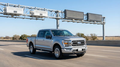 A modern car rental drives under a highway toll gantry on a bright, sunny day in Texas