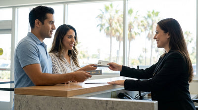 A driver and passenger smile in their car rental on a sunny Los Angeles street lined with palm trees
