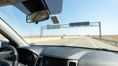 A car rental drives towards an electronic toll booth on a multi-lane highway in Texas under a clear blue sky