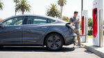 A white Tesla car rental plugged into a Supercharger station on a sunny day in California