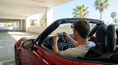 A person photographs the dashboard of a car rental with a smartphone in a sunny Los Angeles parking lot