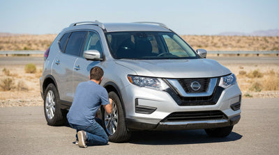 A silver car hire driving on a desert highway in the United States with mountains in the distance