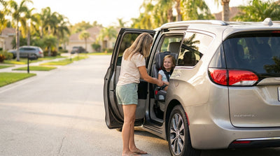A parent secures their child in a booster seat in the back of a car rental on a sunny Florida day