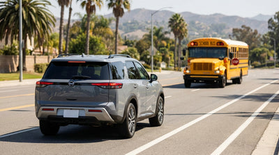 A car hire stopped behind a yellow school bus with flashing red lights on a sunny California road