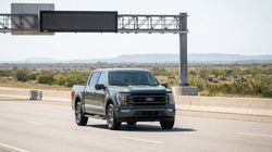 Silver car hire driving under an overhead electronic toll gantry on a sunny Texas highway