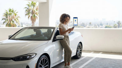A person uses a smartphone to pay for parking next to their car rental on a sunny Los Angeles street