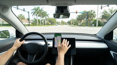 A driver in a car rental uses a phone for navigation while stopped at a traffic light on a sunny Florida street