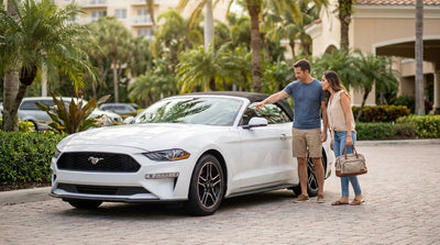 A red convertible car hire driving down a sunny coastal road lined with palm trees in Florida
