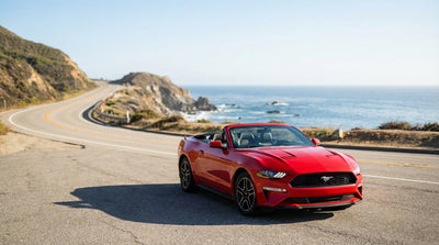 A convertible car hire drives down a winding coastal highway in California on a sunny day
