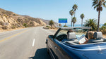 A modern car rental on a scenic California highway, driving through a vast desert landscape toward the horizon