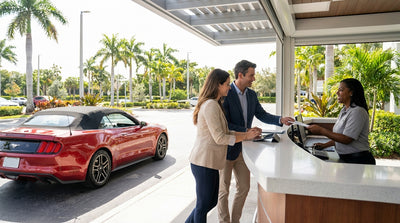 A convertible for car hire drives down a sunny, palm-lined coastal road in Florida