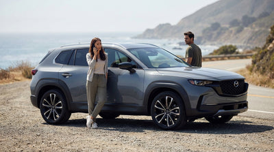A concerned driver looks at their phone while standing next to their car rental on a roadside in the United States