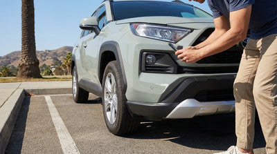 A person kneels to photograph a paint scuff on their California car hire in a sunny parking lot