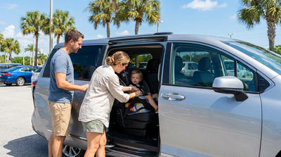 Parent buckling a smiling toddler into a car seat in the back of a family car rental in sunny Florida